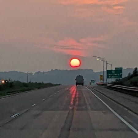 Highway with an orange sky and bright orange setting sun ahead